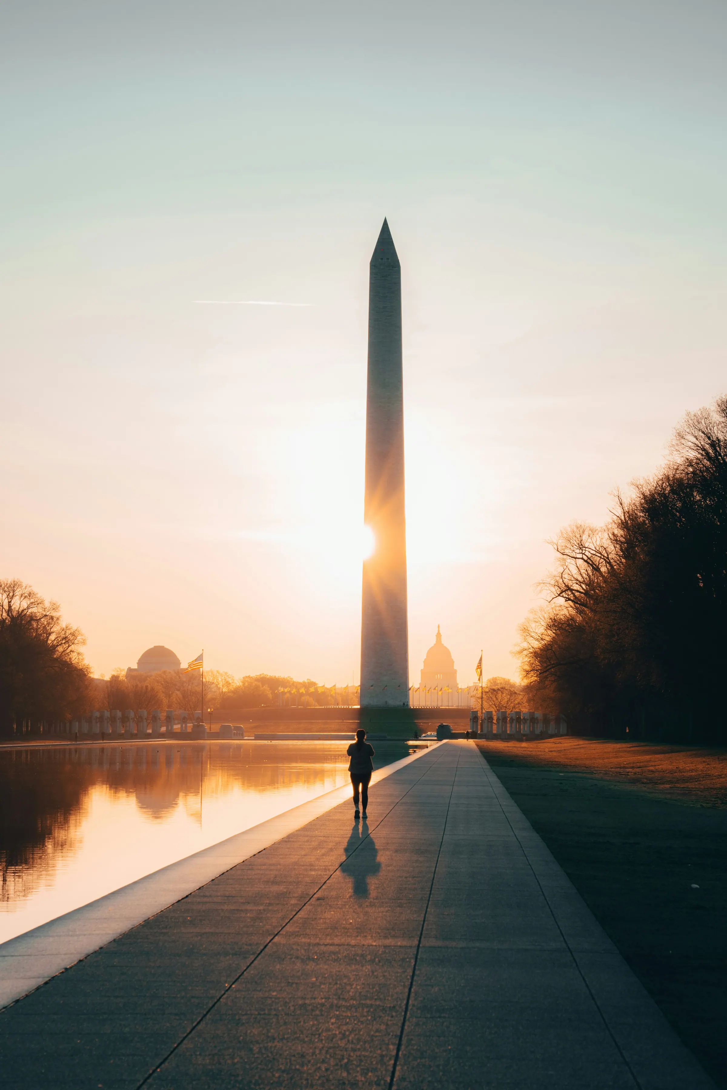 The Washington Monument at sunrise from the Reflecting Pool, a lone walker on the path